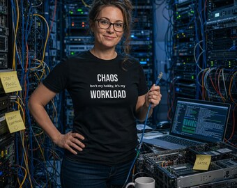 Op de afbeelding: Een zwart t-shirt met de witte tekst 'CHAOS Isn't my hobby, It's my WORKLOAD' op de borst. Het t-shirt wordt gedragen met een donkerblauwe spijkerbroek. Een witte keramische mok met de tekst 'I TURN COFFEE INTO UPTIME' staat op een server.