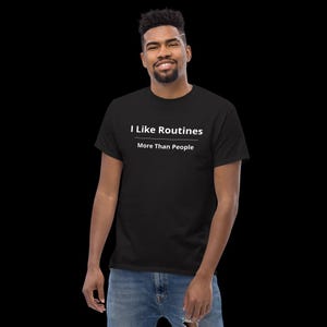 K&ouml;nnte beinhalten: Ein schwarzes kurz&auml;rmeliges T-Shirt mit dem wei&szlig;en Text I Like Routines More Than People auf der Brust. Das Design enth&auml;lt eine horizontale wei&szlig;e Linie, die die beiden S&auml;tze voneinander trennt und mittig auf der Vorderseite platziert ist.