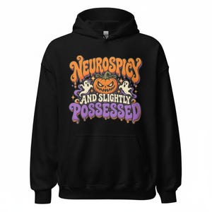 May include: A black hooded sweatshirt featuring a graphic print with the text "NEUROSPICY AND SLIGHTLY POSSESSED". The design includes an orange jack-o'-lantern, two white ghosts, and small stars in orange and purple colors.
