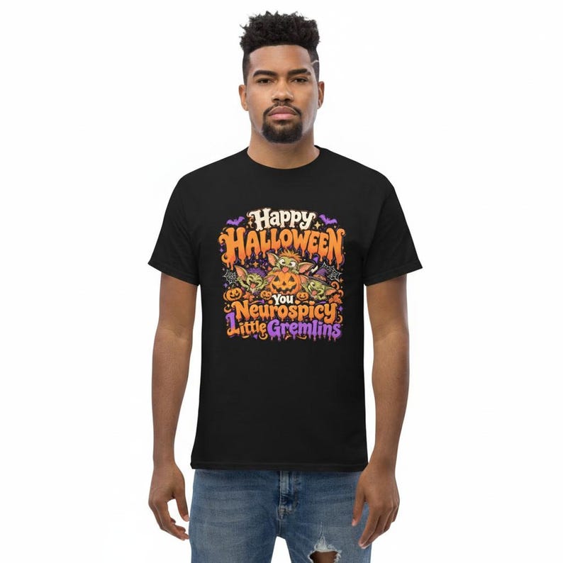 May include: A black t-shirt featuring a colorful Halloween graphic with three green creatures and pumpkins. The text reads Happy Halloween You Neurospicy Little Gremlins in orange and purple lettering, surrounded by bats and spider web accents.