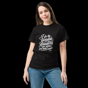 May include: A black short-sleeved t-shirt featuring white text printed on the chest that reads, I fix the invisible disasters you swear you didn't cause, written in a stylised cursive and block font combination on a plain black background.