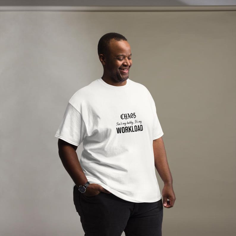May include: A white short-sleeved t-shirt featuring black text printed on the chest that reads: CHAOS Isn't my hobby. It's my WORKLOAD. The shirt has a crew neckline and a standard fit, paired with black trousers and a black wristwatch on the wrist.