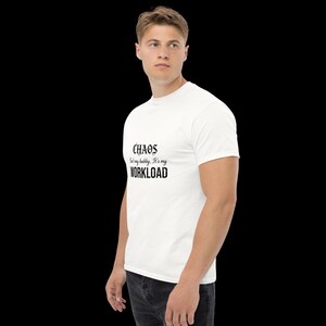 May include: A white short-sleeved t-shirt featuring black text on the chest that reads: CHAOS isn't my hobby, It's my WORKLOAD. The shirt has a crew neckline and a standard fit, presented against a plain black background for clear visibility.