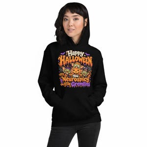 May include: A black hooded sweatshirt featuring a colourful graphic print with the text Happy Halloween You Neurospicy Little Gremlins. The design includes three small green creatures, orange pumpkins, purple bats, and spider webs in a cartoon style.