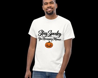 May include: A white short-sleeved t-shirt featuring the black text Stay Spooky You Neurospicy Menace printed on the chest. Below the text is a small, orange, illustrated jack-o'-lantern pumpkin with a jagged, smiling face and green stem.