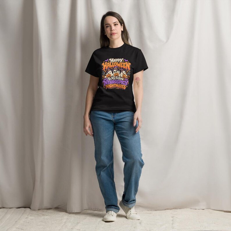 May include: A black short-sleeved t-shirt featuring a colourful graphic print with the text Happy Halloween To My Fellow Neurospicy Nightmares, accompanied by illustrations of ghosts wearing witch hats and holding orange pumpkins, paired with blue jeans.