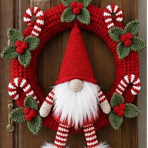Op de afbeelding: Een gehaakte kerstkrans met een centrale kabouter met een hoge rode muts, een witte baard en gestreepte benen. De rode ronde krans is versierd met gehaakte groene hulstblaadjes, rode bessen en rood-witte zuurstokken.
