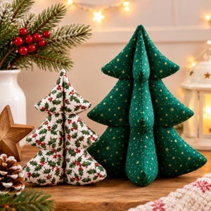 Puede incluir: Dos adornos de árbol de Navidad de tela. Un árbol es blanco con un patrón de hojas de acebo verdes y bayas rojas. El segundo árbol es verde oscuro con un estampado de estrellas doradas. Ambos tienen una estructura acolchada y tridimensional.