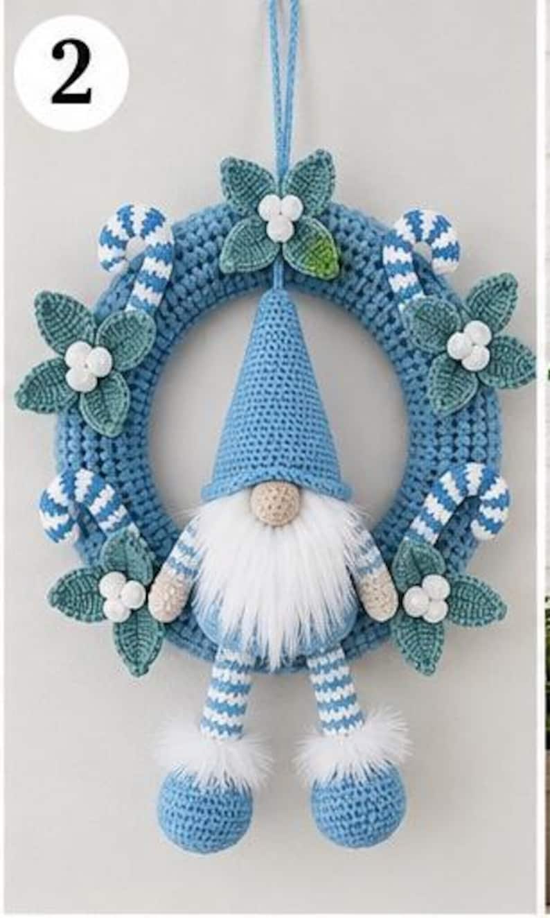 Op de afbeelding: Een blauwe gehaakte krans met een centrale kabouter met een hoge blauwe muts, een witte baard van imitatiebont en gestreepte benen. De krans is versierd met gehaakte groene bladeren, witte bessen en blauw-wit gestreepte zuurstokken.