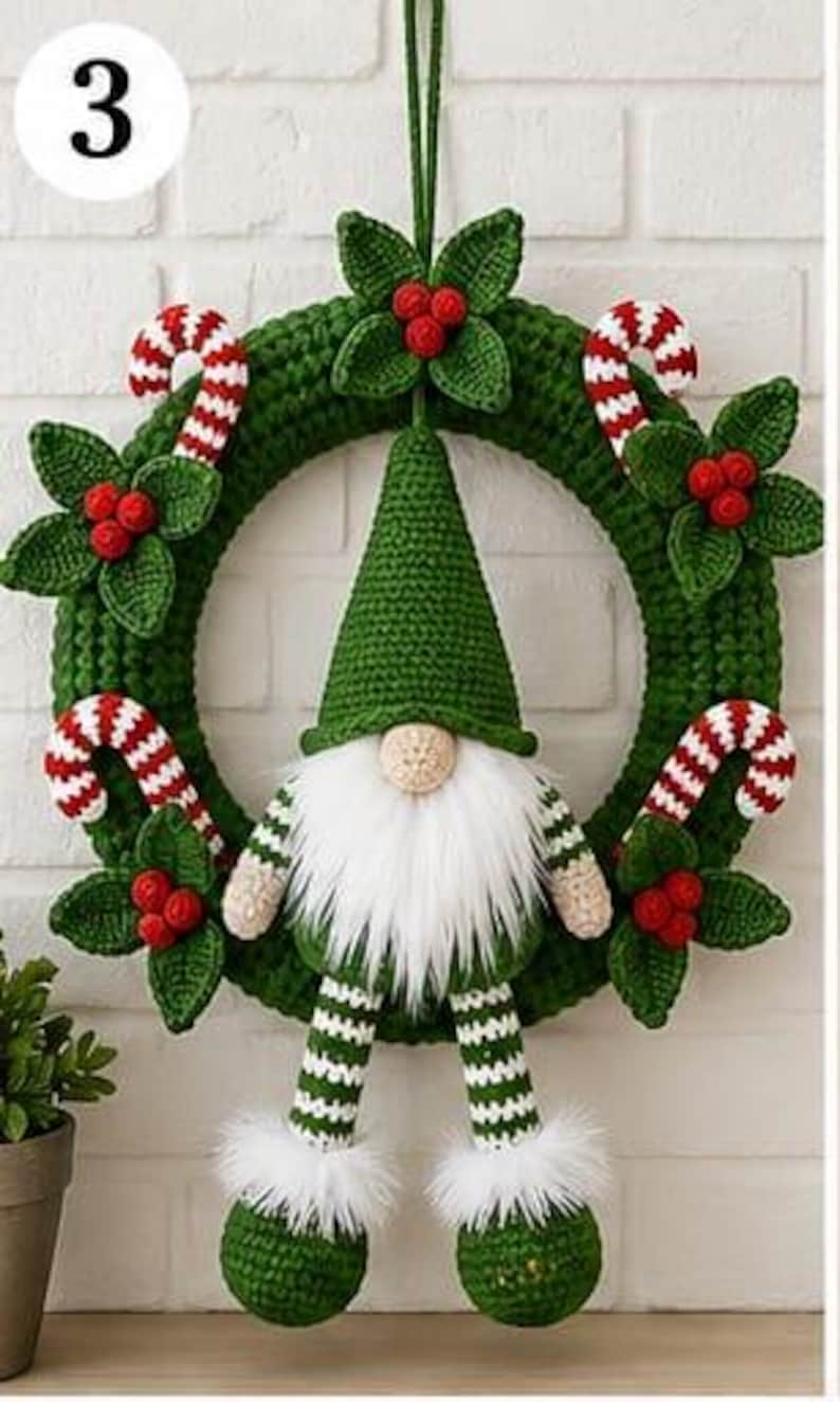 Op de afbeelding: Een gehaakte groene krans met een centrale kabouter met een hoge groene muts, witte baard en gestreepte benen. De krans is versierd met rood-witte zuurstokken en trossen groene bladeren met kleine rode bessen die eraan bevestigd zijn.
