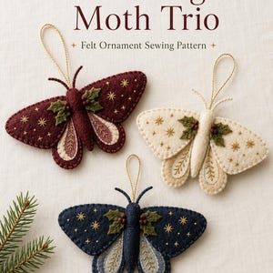 May include: Three felt moth ornaments with gold hanging loops, featuring embroidered star patterns, green holly leaves, and red berries. The moths are in deep burgundy, cream, and navy blue. Text reads: Dreamy Yarn Studio Winter Night Moth Trio.