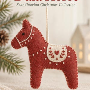 May include: A red felt Dala horse ornament with white stitched details, a cream-colored saddle patch featuring a small red heart, and a white hanging string. The text reads Dala Horse, Scandinavian Christmas Collection, and Dreamy Yarn Studio.