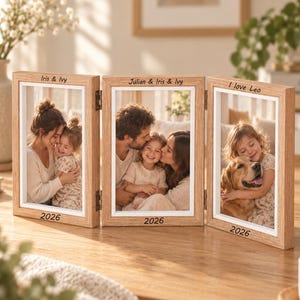 May include: A light wood triptych photo frame with three hinged panels. Each frame features white inner borders and engraved text: 'Iris & Ivy', 'Julian & Iris & Ivy', and 'I love Leo' at the top, with '2026' engraved at the bottom of each frame.