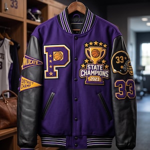 Könnte beinhalten: Eine violette College-Jacke mit schwarzen Lederärmeln, verziert mit einem großen Buchstaben P, einer Trophäengrafik mit dem Text STATE CHAMPIONS 2023 sowie Wimpeln mit der Aufschrift WILDCATS und DISTRICT CHAMP. Die Ärmel zeigen die Nummer 33 und einen Helm.