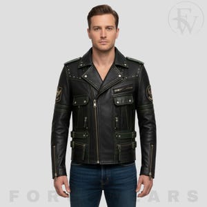 Könnte beinhalten: Eine schwarze Lederjacke mit Reverskragen und silbernen Nieten, diagonalem Frontreißverschluss, mehreren Reißverschluss- und Pattentaschen, verstellbaren Seitengurten mit Schnallen sowie runden Aufnähern an beiden Schultern über blauen Jeans.