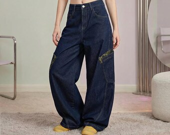 Puede incluir: Pantalones cargo de mezclilla azul oscuro de tiro alto, con cierre de botón y cremallera, piernas anchas y bolsillos laterales con detalles de estampado de camuflaje. Los pantalones se combinan con zapatillas amarillas y un top corto.