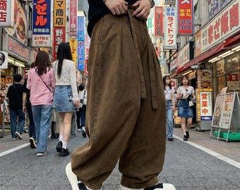 Puede incluir: Pantalones marrones de corte holgado y cintura alta, con cinturón de tela a juego, detalles de pliegues frontales y perneras anchas, combinados con zapatillas de plataforma blancas con detalles negros en la puntera y el talón.