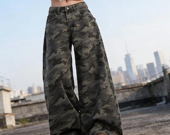 Puede incluir: Pantalones vaqueros de tiro alto y pernera ancha con un estampado de camuflaje en tonos verde oscuro, marrón y negro. Los pantalones incluyen cierre de botón y cremallera, trabillas para cinturón y dos bolsillos delanteros.