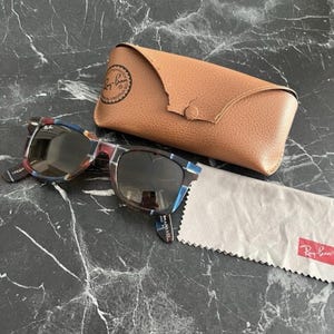 Puede incluir: Gafas de sol Ray-Ban con montura de carey multicolor con detalles en azul y marr&oacute;n, lentes oscuras, un estuche protector de cuero color canela con cierre de broche y un pa&ntilde;o de limpieza de microfibra gris claro con el logo de Ray-Ban.