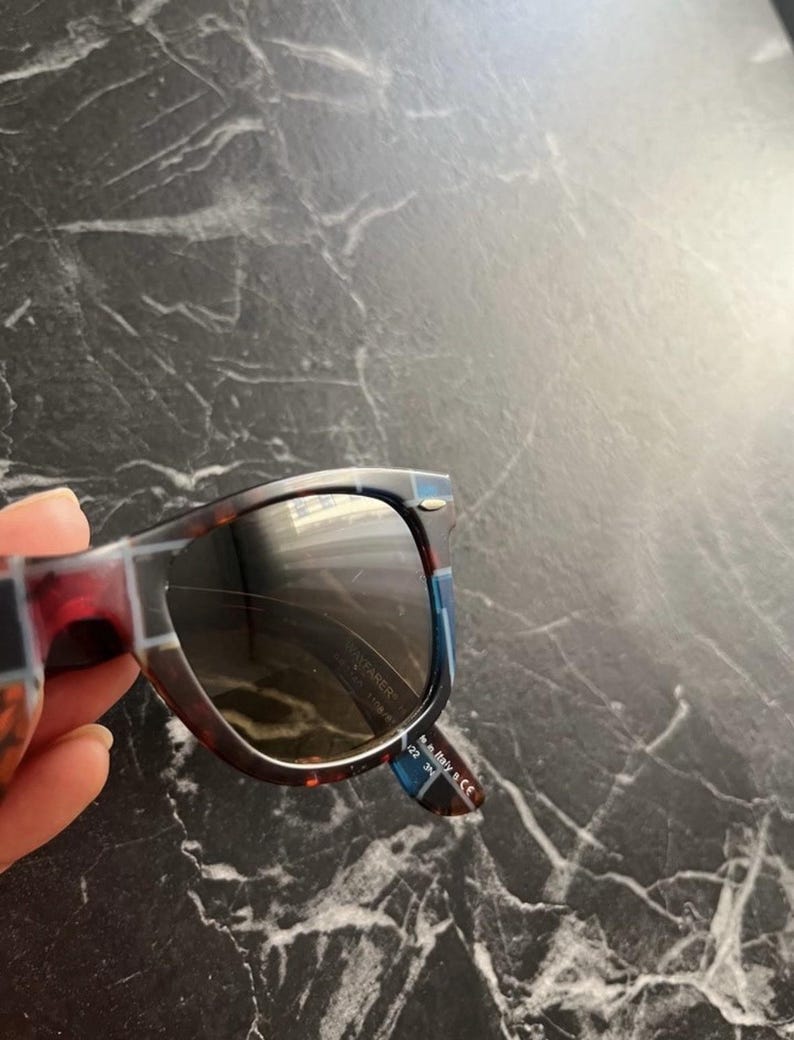 Puede incluir: Gafas de sol de carey con montura estampada en azul y marr&oacute;n oscuro. La patilla interior presenta el texto blanco Made in Italy 5 CE y 122 3N. Las lentes est&aacute;n tintadas en oscuro y la montura incluye un peque&ntilde;o detalle met&aacute;lico plateado.
