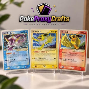 Op de afbeelding: Drie Japanse ruilkaarten op doorzichtige standaards. De linkerkaart is blauw met een paars wezen, de middelste kaart is geel met een geel wezen en de rechterkaart is rood met een oranje wezen. Elke kaart bevat de tekst HP70.