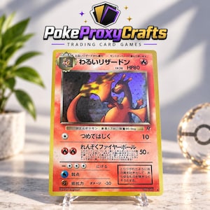 Pode incluir: Uma carta colecionável japonesa Dark Charizard com uma ilustração holográfica da criatura do tipo fogo. A carta exibe o nome, 80 HP, movimentos de ataque e texto em japonês. É apresentada num suporte transparente com o logótipo PokeProxyCrafts.