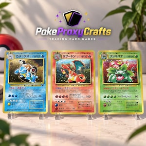 Può includere: Tre carte collezionabili con bordo dorato raffiguranti Blastoise, Charizard e Venusaur con testo in giapponese. Ogni carta mostra un'illustrazione, valori HP e statistiche di attacco. Le carte sono posizionate su supporti in plastica trasparente.