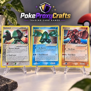 May include: Three trading cards featuring Registeel, Regice, and Regirock displayed on clear plastic stands. Each card shows a character illustration, 90 HP, and text detailing attacks like Barrier Attack, Ice Barrier, and Dig Drain.