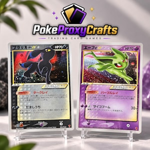 Peut inclure: Deux cartes à collectionner rectangulaires présentées sur des supports en plastique transparent. La carte de gauche montre un personnage Umbreon noir avec des accents bleus sur un fond étoilé. La carte de droite montre un personnage Espeon vert.