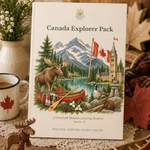 May include: A white book titled Canada Explorer Pack featuring a detailed illustration of a moose, a red canoe, a Canadian flag, a stone building, a goose, and a beaver in a mountain landscape. The text reads A Storybook Meadow Learning Resource Ages 6-11 and DISCOVER EXPLORE LEARN CREATE.