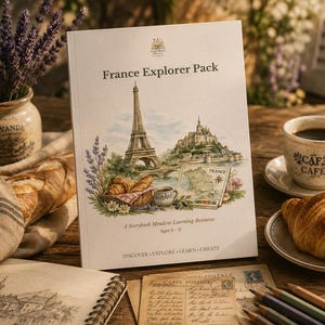 Könnte beinhalten: Ein weißes Lernheft mit dem Titel France Explorer Pack, das eine Aquarellillustration des Eiffelturms, des Mont Saint-Michel, einer Frankreichkarte und Croissants zeigt. Der Einband enthält den Text A Storybook Meadow Learning Resource Ages 6-11.