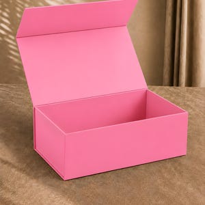 Könnte beinhalten: Eine rechteckige, leuchtend rosa Geschenkbox mit einem geöffneten Klappdeckel. Die Box hat eine glatte, einfarbige Außen- und Innenseite sowie eine klare Konstruktion mit einem stabilen, aufrechten Deckel zur Aufbewahrung oder Präsentation.