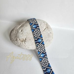 Könnte beinhalten: Ein Perlenarmband mit einem geometrischen Muster in Blau-, Schwarz- und Weißtönen. Das Design besteht aus sich wiederholenden Rautenformen und kantigen Linien. Der Text Agat888 ist in der unteren linken Ecke des Bildes zu sehen.