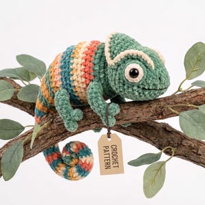 May include: A crocheted chameleon toy featuring a textured green head and a body with horizontal stripes in shades of teal, orange, yellow, and cream. The toy has a curled tail and a small rectangular tag attached that reads CROCHET PATTERN.