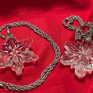 May include: Two silver chains with crystal snowflake pendants. The snowflakes are clear and have a faceted design.