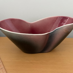 May include: A pink and black ceramic bowl with a unique, organic shape. The bowl has a smooth, glossy finish and is perfect for serving snacks or holding decorative items.