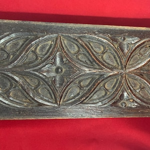 May include: A dark brown wooden panel with intricate carved floral designs. The panel has a distressed look and is likely antique.