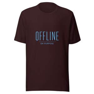 Peut inclure: Un t-shirt à manches courtes marron foncé avec le texte "OFFLINE" en grandes lettres capitales bleu clair, une ligne horizontale en dessous et les mots "ON PURPOSE" en plus petites lettres capitales bleu clair centrés sous la ligne.