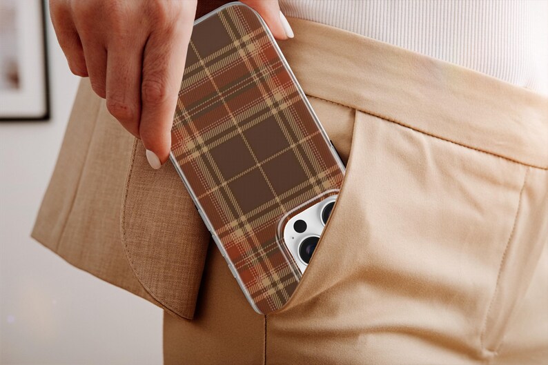 May include: A smartphone case featuring a brown, tan, and orange plaid pattern. The case has a rectangular shape with rounded corners and a cutout for the camera lens array, showing the white back of the phone and black camera lenses.