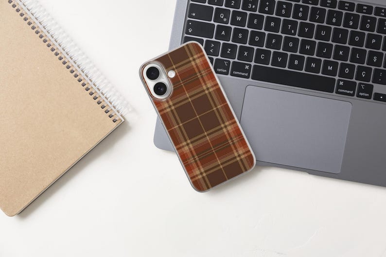 May include: A smartphone case featuring a brown, orange, and cream plaid pattern. The case has a clear border and cutouts for the dual camera lenses and flash. The design covers the entire back of the phone, showcasing a classic tartan grid.