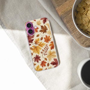May include: A clear smartphone case featuring a repeating pattern of autumn maple leaves in shades of yellow, orange, and deep red, accented with small clusters of brown berries. The case has a distinct purple circular camera lens frame.