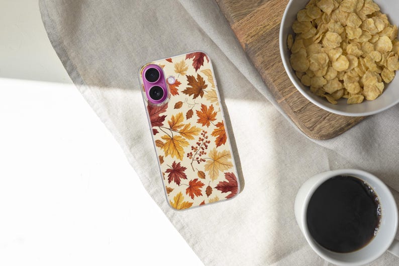 May include: A clear smartphone case featuring a repeating pattern of autumn maple leaves in shades of yellow, orange, and deep red, accented with small clusters of brown berries. The case has a distinct purple circular camera lens frame.