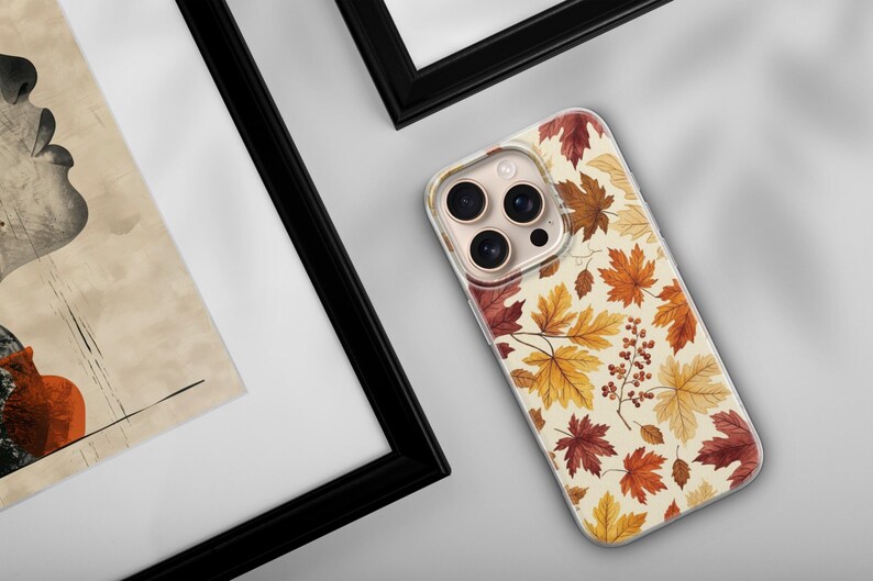 May include: A clear smartphone case featuring a repeating pattern of autumn maple leaves in shades of red, orange, and yellow, interspersed with small clusters of brown berries against a cream-colored background, shown on a device with three lenses.