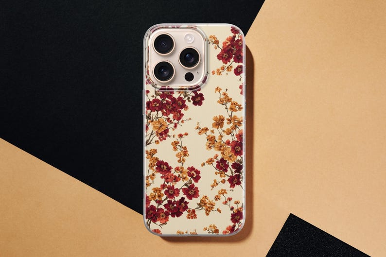 May include: A clear smartphone case featuring a floral pattern with deep red and golden yellow blossoms on thin brown branches. The design is set against a cream-colored background, covering the back of a smartphone with a triple-lens camera system.