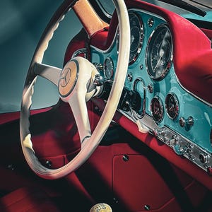 May include: The interior of a vintage vehicle featuring a cream-colored steering wheel with a central Mercedes-Benz emblem, a bright turquoise dashboard with circular analog gauges, red upholstery, and a cream-colored gear shift knob.