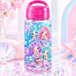 May include: A clear plastic water bottle with a bright pink lid and handle. The bottle features a colourful graphic print of four mermaids with blue, pink, purple, and teal hair, surrounded by sea creatures, a treasure chest, and coral reefs.