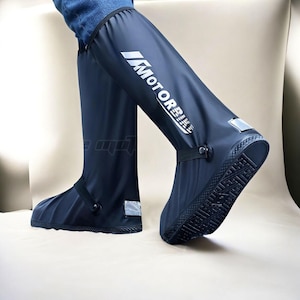 May include: A pair of knee-high black waterproof shoe covers featuring the white text MOTORBIKE printed vertically on the side. These protective covers have a textured black rubber sole, a snap button strap across the midfoot, and reflective accents.