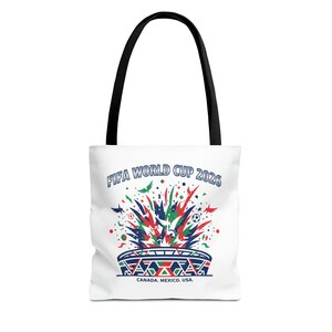 Könnte beinhalten: Eine weiße Tragetasche mit schwarzen Henkeln und einer bunten Grafik eines Stadions mit einer Explosion aus roten, grünen und blauen Formen. Der Text lautet oben FIFA WORLD CUP 2026 und unten CANADA. MEXICO. USA. auf der Grafik.