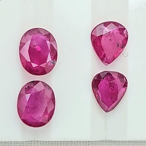 Puede incluir: Cuatro piedras preciosas facetadas con un tono magenta rosado intenso. Dos de las piedras tienen forma ovalada, mientras que las otras dos tienen forma de pera. Cada piedra presenta una superficie pulida con múltiples facetas geométricas.