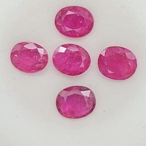 Può includere: Cinque rubini rosa vibrante dal taglio ovale disposti a croce. Ogni gemma presenta una superficie sfaccettata che riflette la luce, mostrando una profonda tonalità magenta e un aspetto lucido e traslucido su tutte e cinque le pietre.